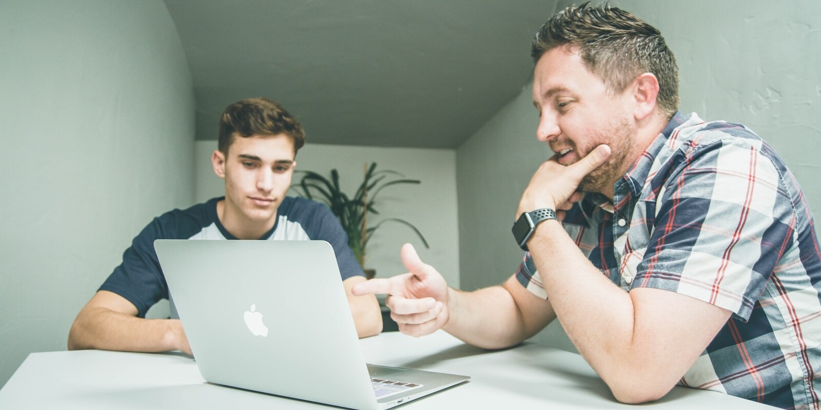 man wearing white and black plaid button-up sports shirt pointing the silver MacBook